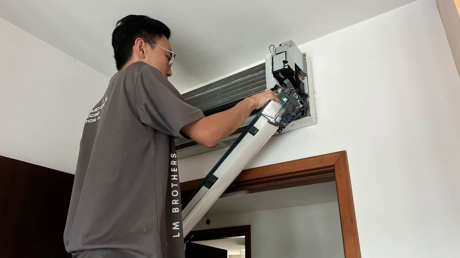 LM Brothers technician on a step ladder servicing a wall-mounted aircon unit