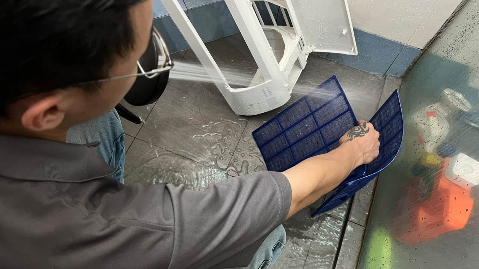 LM Brothers technician washing out an aircon filter at the drain after taking it off the unit