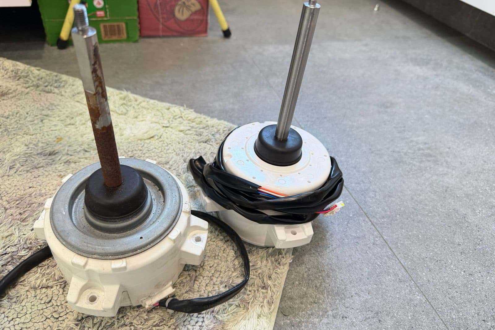 A removed aircon fan motor with a rusted shaft beside its clean replacement