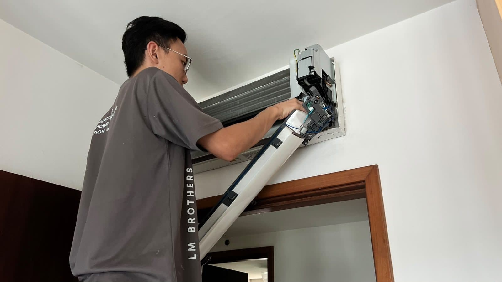 LM Brothers technician working on a wall-mounted indoor unit from a step ladder